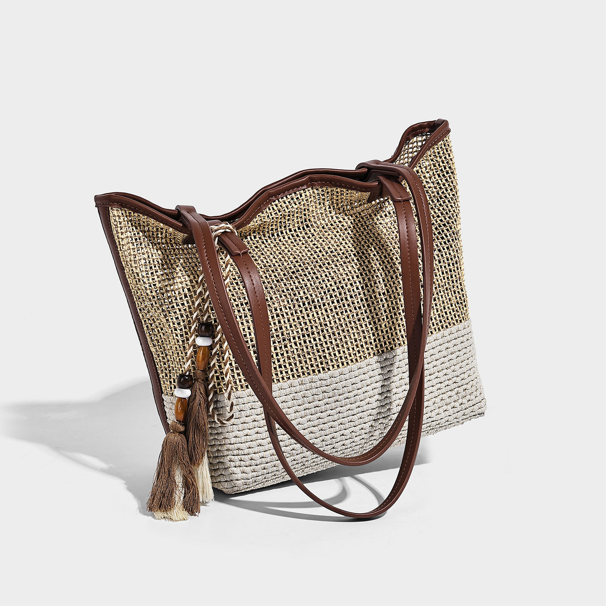 Woven beige and cream tote bag with brown leather-look trim, long double shoulder straps, and knotted tassel charm on front