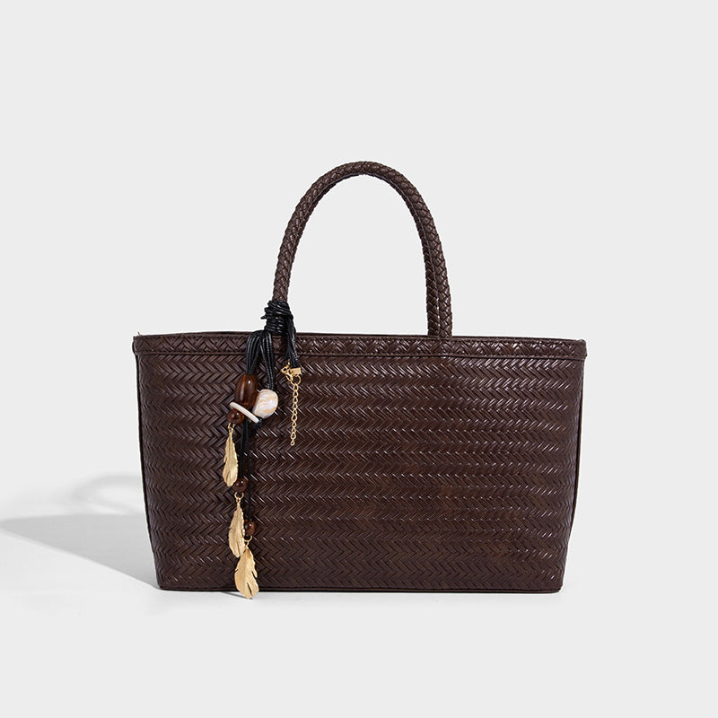 Structured woven-texture tote bag with brown braided top handles, decorative tassel charm, and detachable shoulder strap