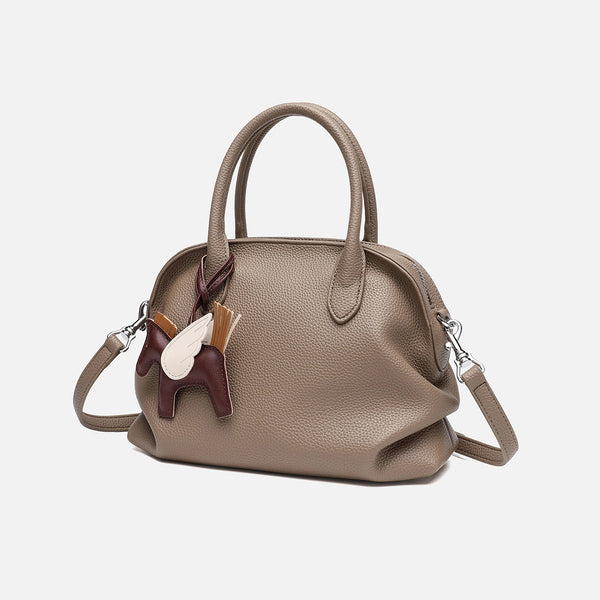 Rounded dome shell handbag in pebbled leather-look finish with twin top handles, zip closure, decorative horse charm, and