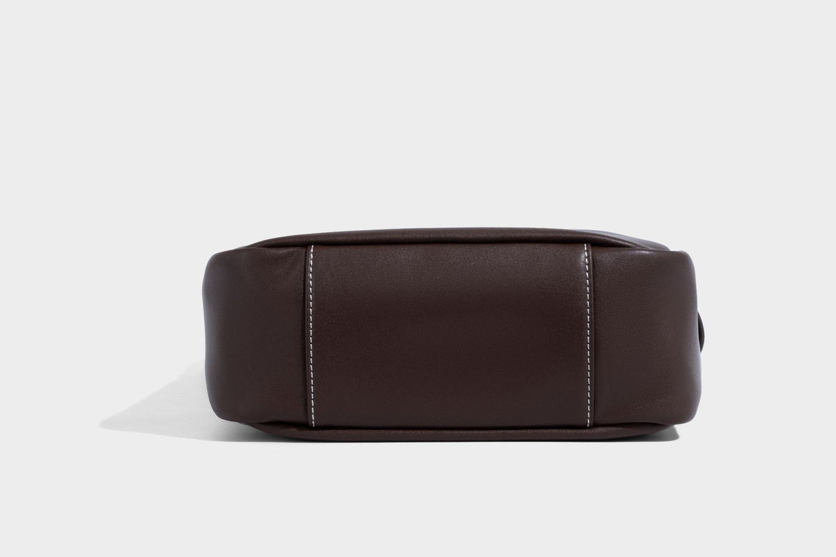 Structured dark brown leather-look bucket bag with white contrast stitching, front wraparound belt buckle strap, and long