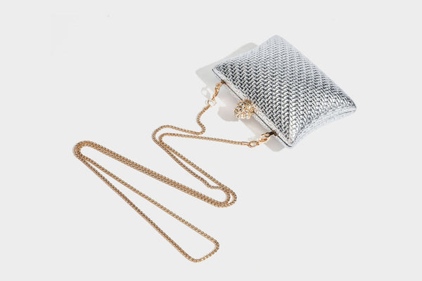 Small structured rectangular metallic woven-texture clutch bag with jeweled knob clasp and gold-tone chain strap, detail view