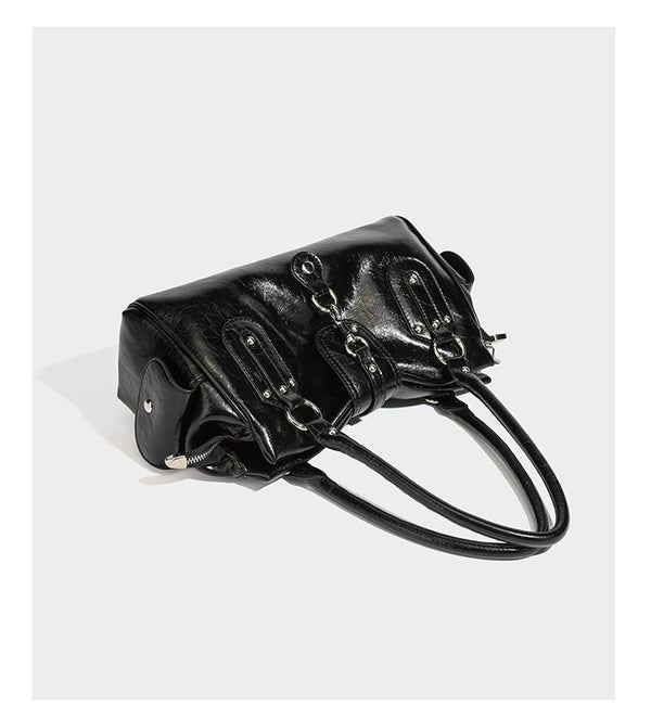 Glänzende, geknautschte Barrel-Satchel mit zwei oberen Tragegriffen, vorderem Klappen-Riemen-Panel, Ring- und Nietenbeschlägen sowie einem abnehmbaren