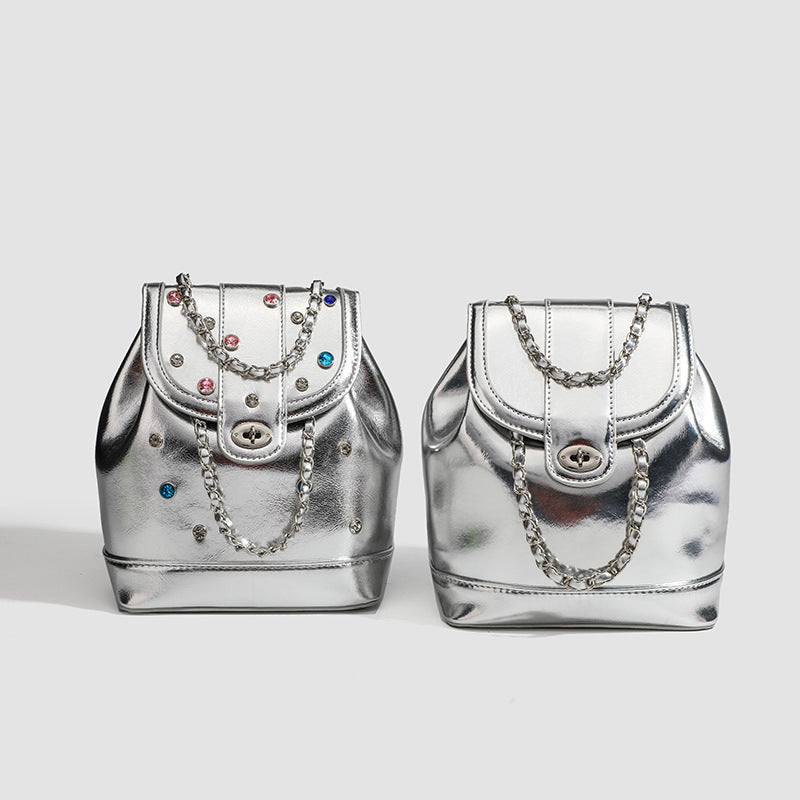 Compact silver metallic backpack handbag with multicolour crystal studs, round turn-lock flap closure, and interwoven silver