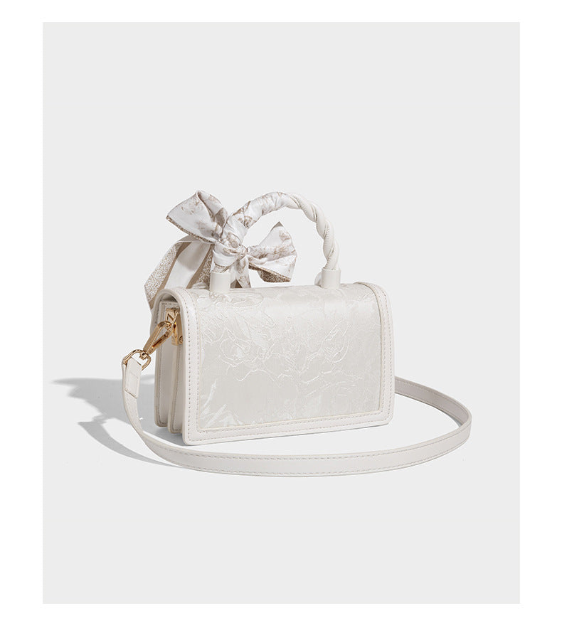 Small structured white flap bag with butterfly embroidery, flower-shaped turn-lock clasp, braided top handle with scarf bow