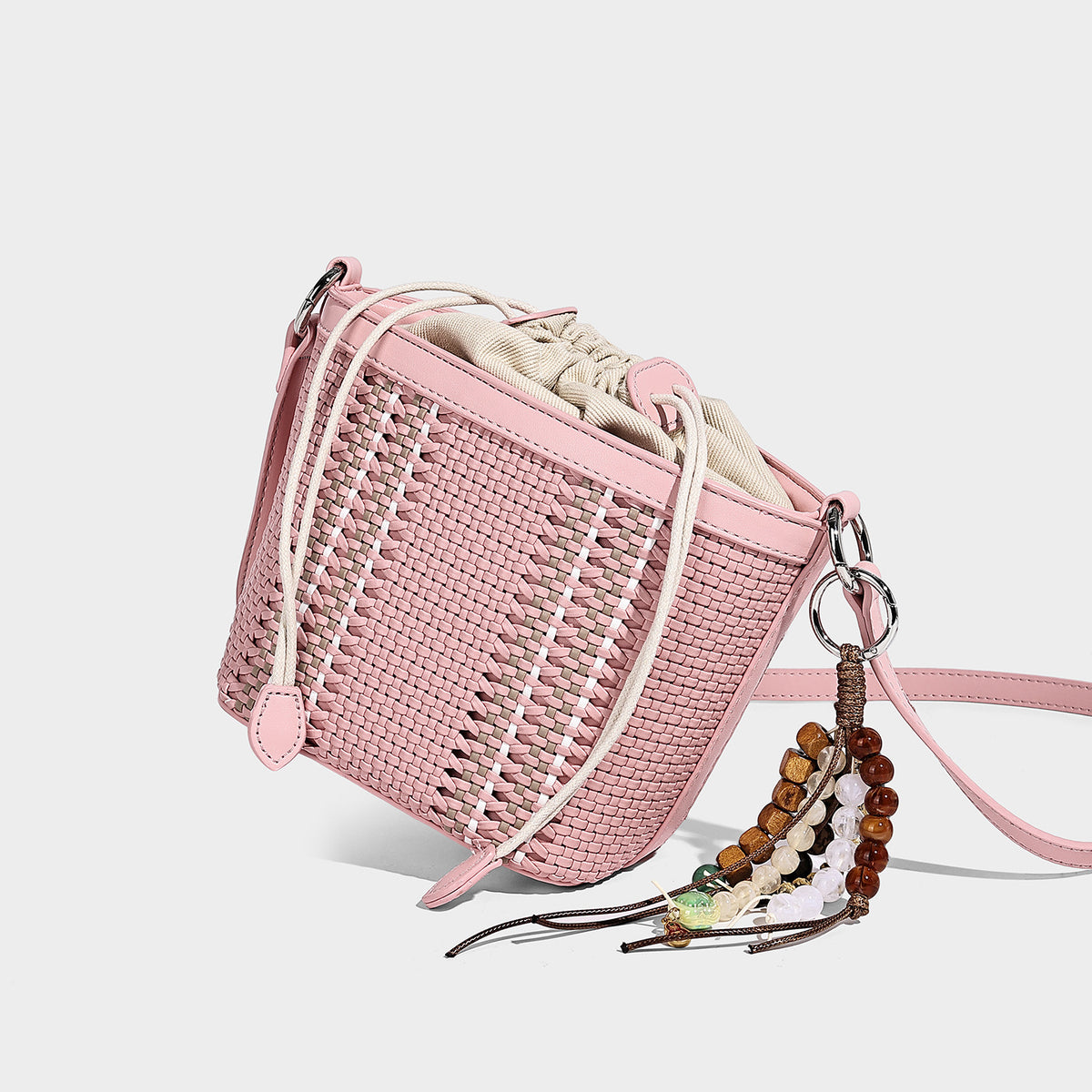 Small woven bucket bag with drawstring top, braided handle, detachable crossbody strap, and silver-tone ring hardware, detail