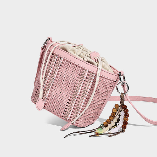 Small woven bucket bag with drawstring top, braided handle, detachable crossbody strap, and silver-tone ring hardware, detail
