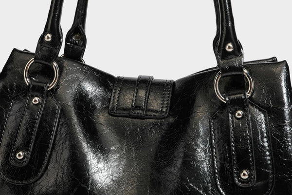 Glänzende, geknautschte Barrel-Satchel mit zwei oberen Tragegriffen, vorderem Klappen-Riemen-Panel, Ring- und Nietenbeschlägen sowie einem abnehmbaren