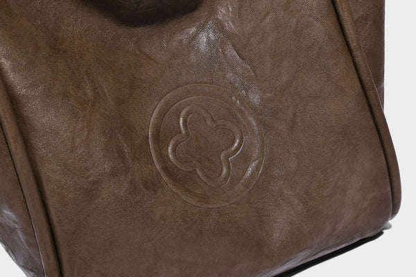 Glänzende Tragetasche in geknautschtem Lederlook mit geprägtem kreisförmigem Emblem, Quastenverschluss, zwei Tragegriffen und abnehmbarem