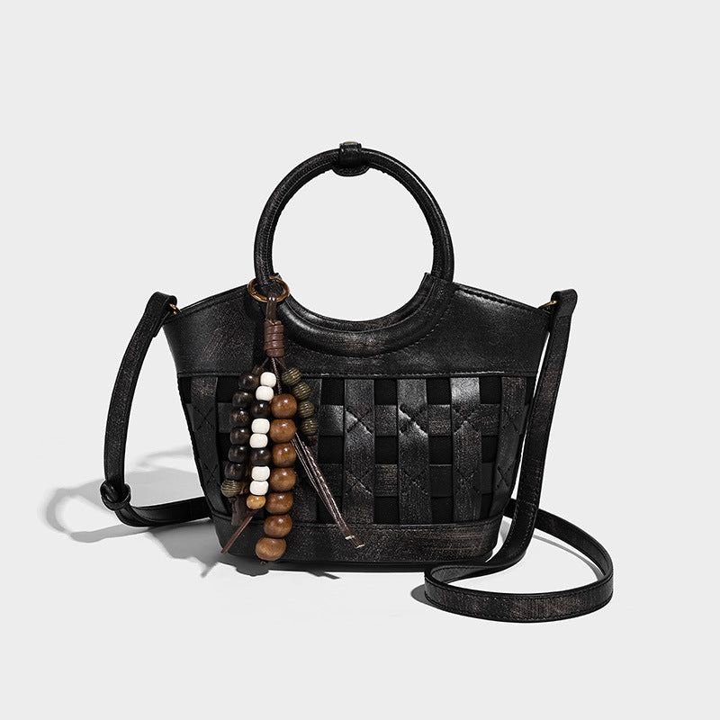 Small woven-panel bucket bag with circular ring handles, beaded tassel charm, and detachable crossbody strap in brown, detail