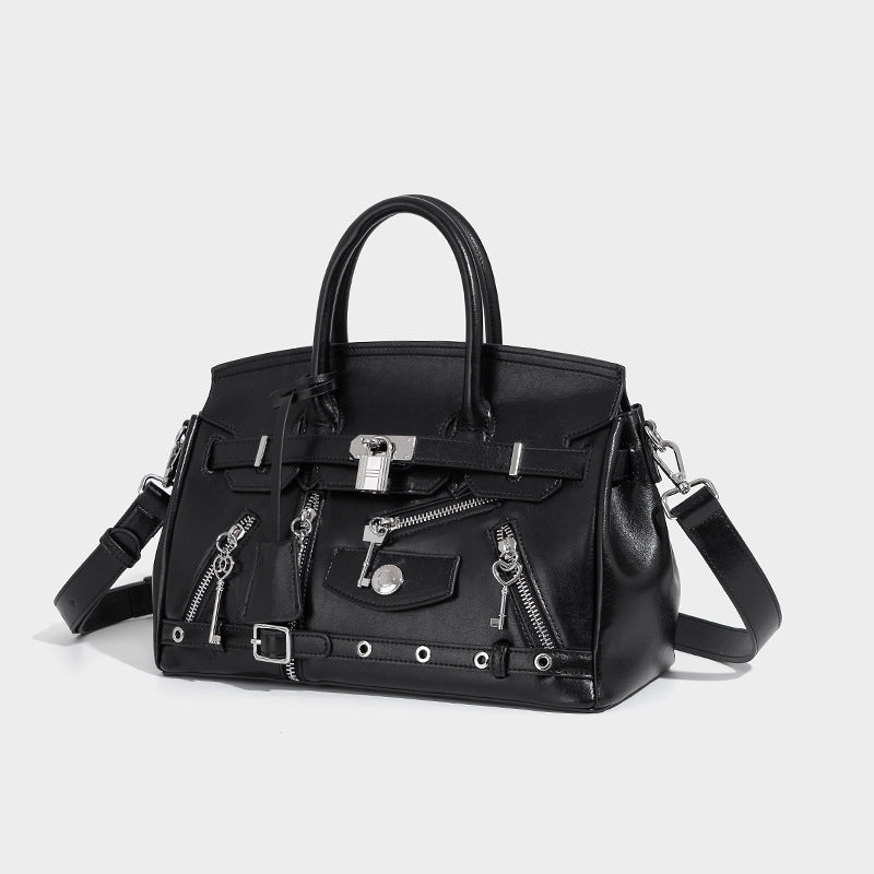 Strukturierte schwarze Henkeltasche in Lederoptik mit silberfarbenem Schloss, vorderen Reißverschlusstaschen, Schlüsselanhängern und Tragegriffen, Vorderansicht