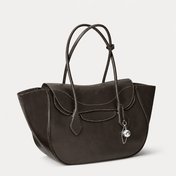 Large winged leather-look tote bag with single arched handle, stitched flap-front panel, and silver ball charm in cognac