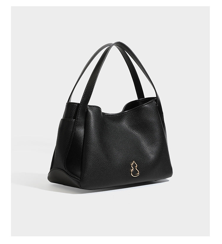 Schwarze Tote-Bag aus genarbtem Material in Lederoptik mit kürbisförmigen Beschlägen in Goldoptik, zwei Henkeln und abnehmbarem Umhängeriemen, Detailansicht