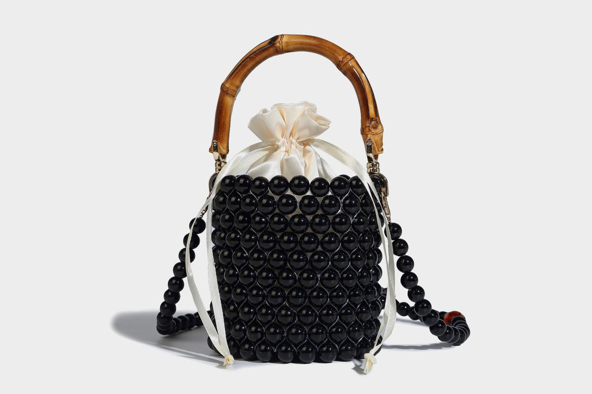 Small cylindrical bucket bag with glossy faux-pearl bead exterior, bamboo arched top handle, satin drawstring closure, and