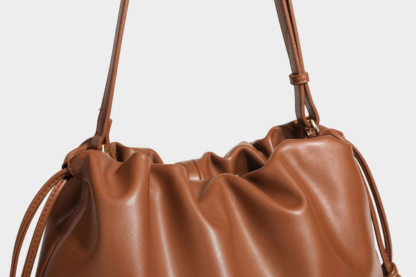 Slouchy ruched drawstring shoulder bag in smooth leather-look finish with gold-tone emblem and slim adjustable strap, detail