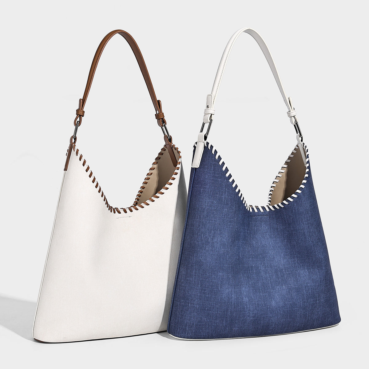 Denim-blue hobo tote with white leather-look shoulder strap, contrast whipstitch trim along curved open top, and silver-tone