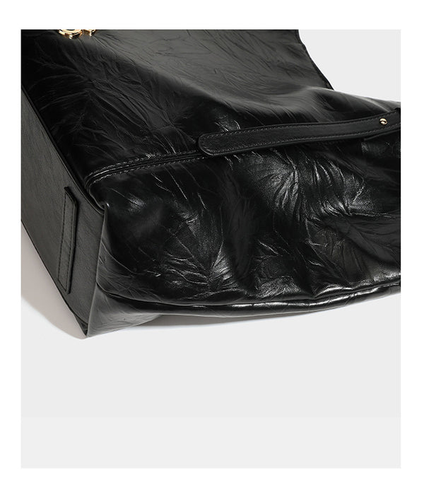 Große, glänzende Tote-Bag aus schwarzem Lederimitat mit geknitterter Optik, lässig fallender Trapezsilhouette, zwei Schulterriemen und goldfarbenen