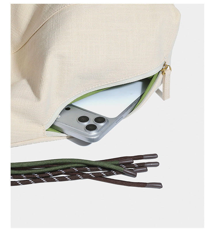 Soft slouchy cream canvas shoulder tote with braided brown and green cord handle, gold-tone ring hardware, and tassel trim