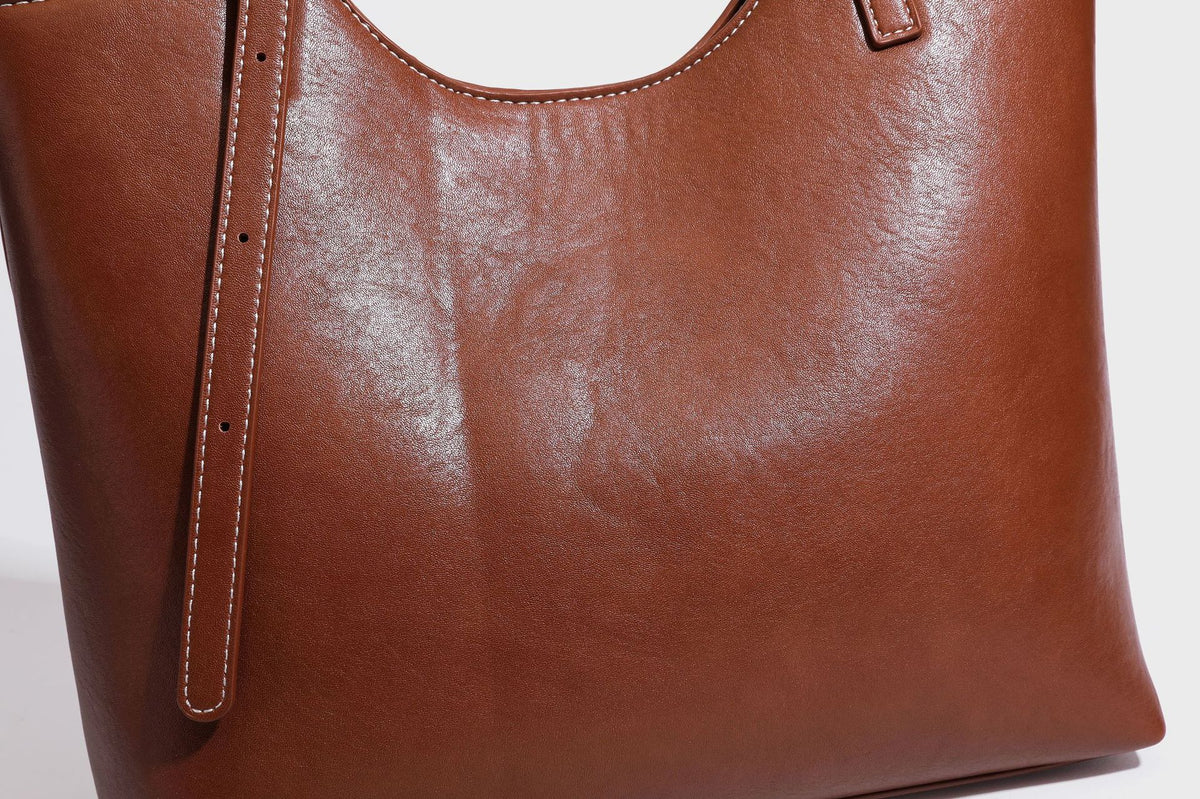 Structured smooth leather-look tote bag with long shoulder strap, gold-tone hardware, and hanging tassel-coin charm, detail