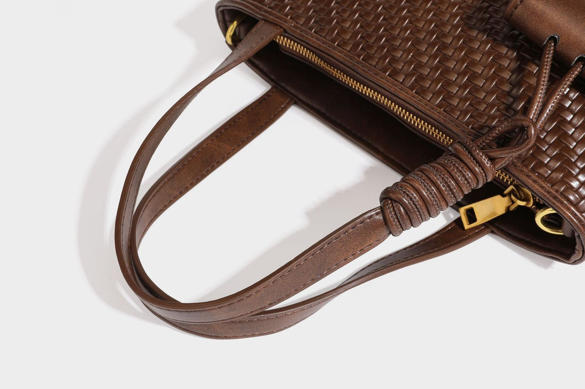 Strukturierte Tote Bag mit gewebter Oberfläche in Braun, goldfarbenen Metalldetails, seilumwickelten Tragegriffen, einer kleinen Fronttasche und weiteren Details