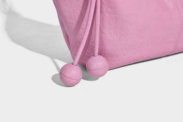Slouchy crescent half-moon shoulder bag in pink pebbled textured finish with floral charm and knotted side detail, detail