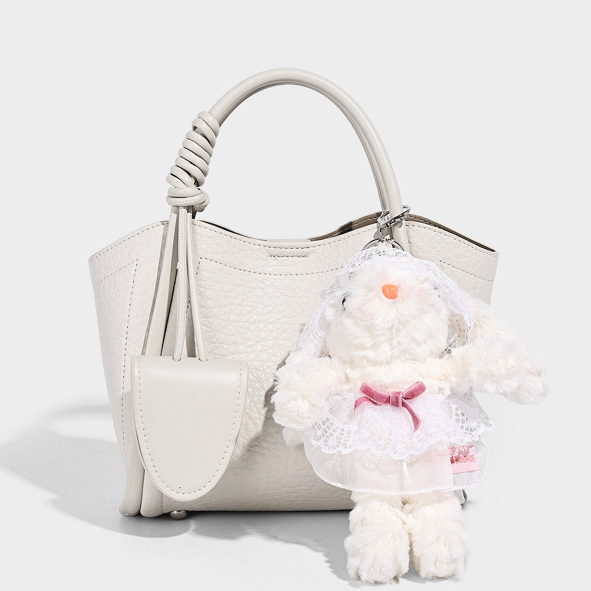 Structured mini tote bag in pebbled leather-look finish with knotted top handles, front flap pocket, and detachable shoulder