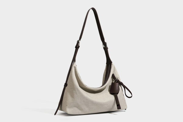 Lässige Hobo-Schultertasche aus haferfarbenem Canvas mit dunkelbraunen Besätzen in Lederoptik, silberfarbenem Reißverschluss und langem, verstellbarem