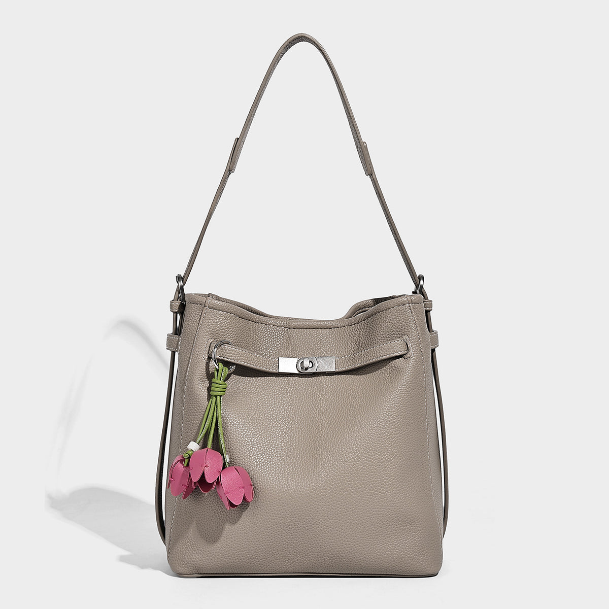 Soft-structured pebbled bucket shoulder bag with front turn-lock strap detail, adjustable strap, and hanging floral tassel