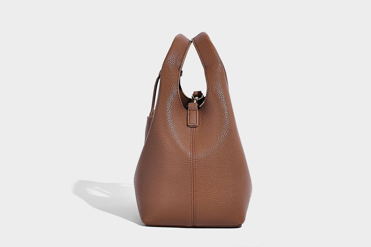 Structured pebbled-texture bucket bag with arched top handles, gold-tone turn-lock closure, and detachable shoulder strap