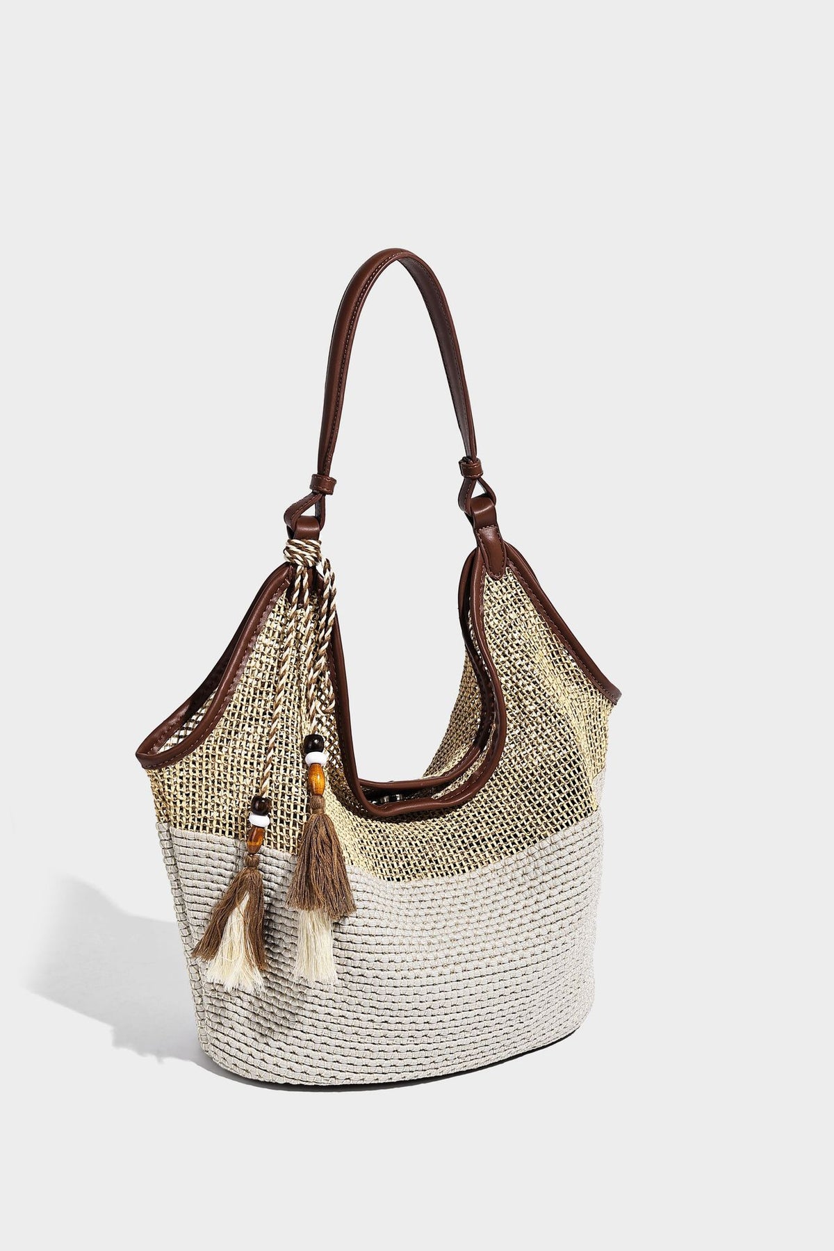 Two-tone beige and cream woven straw hobo shoulder bag with brown leather-look trim, long shoulder strap, and tassel-bead