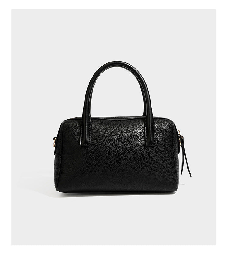 Small structured pillow satchel bag with pebbled leather-look finish, dual rolled top handles, gold-tone gourd emblem, and