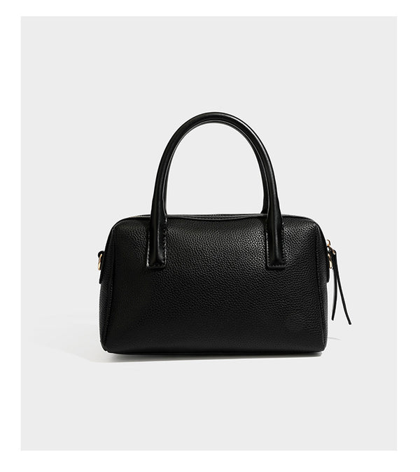Small structured pillow satchel bag with pebbled leather-look finish, dual rolled top handles, gold-tone gourd emblem, and