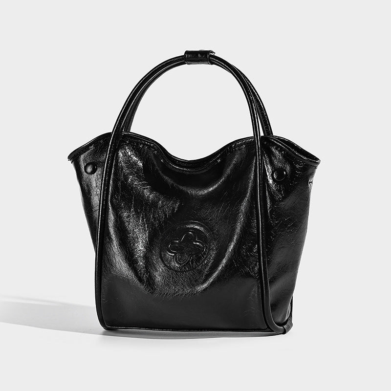 Glossy leather-look structured tote bag with rounded top handles, detachable shoulder strap, embossed front emblem, and side