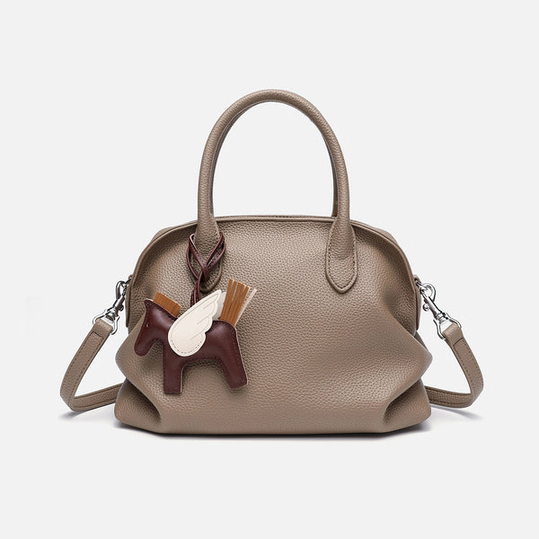 Rounded dome shell handbag in pebbled leather-look finish with twin top handles, zip closure, decorative horse charm, and