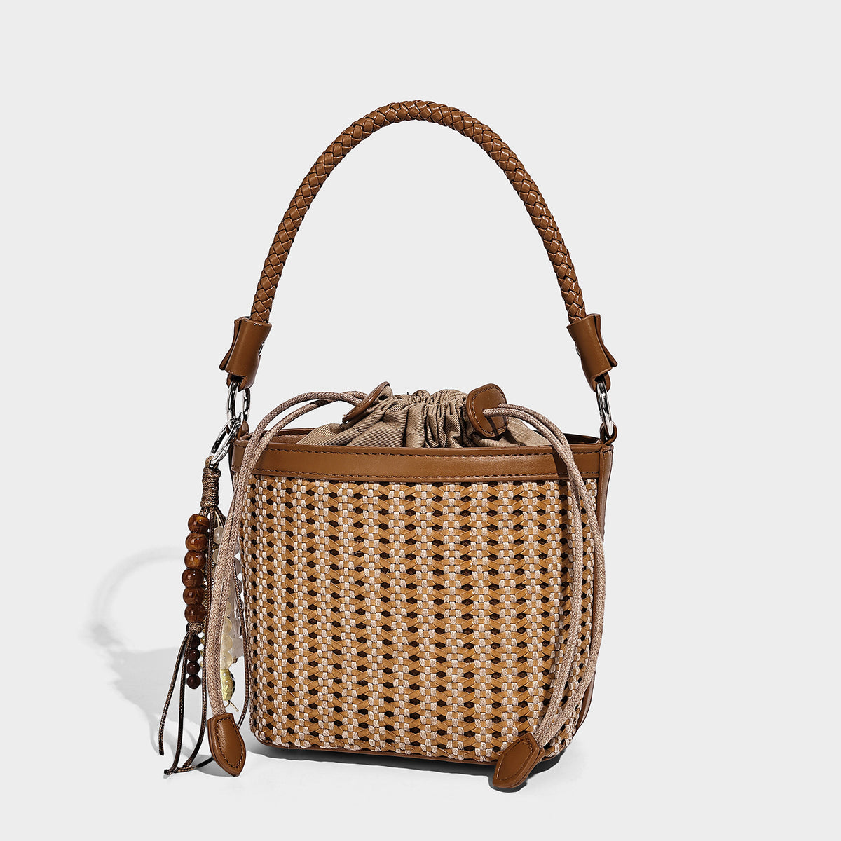 Small woven bucket bag with drawstring top, braided handle, leather-look tan trim, and bead charm tassel, front view