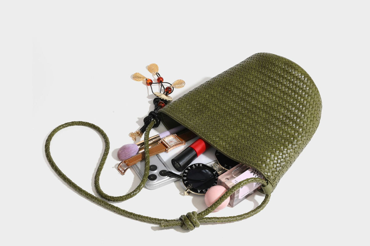 Olive green woven leather-look bucket bag with braided crossbody strap, knotted adjustment, and gold-tone tassel charm with