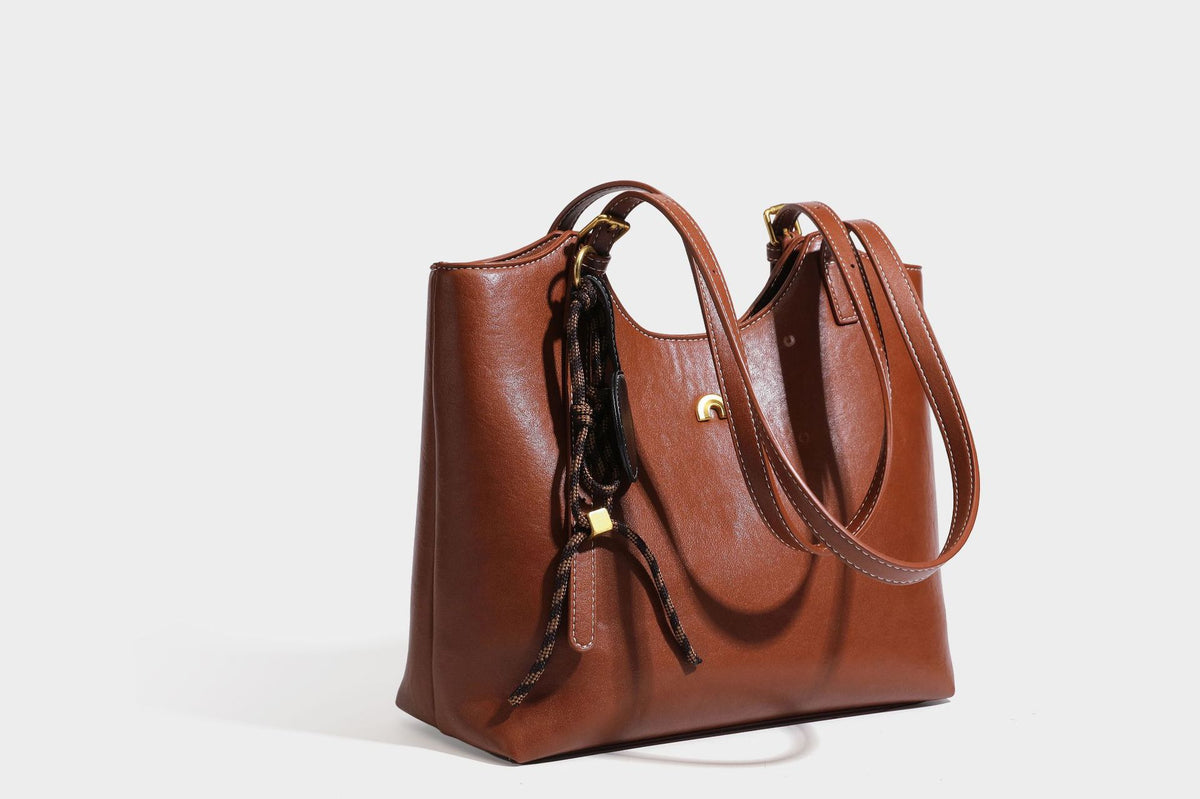 Structured smooth leather-look tote bag with long shoulder strap, gold-tone hardware, and hanging tassel-coin charm, detail