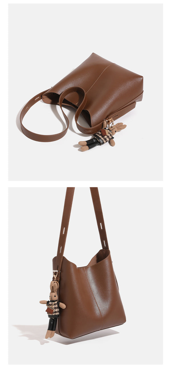 Smooth leather-look bucket bag with long flat shoulder strap, open top, gold-tone hardware, and decorative rabbit charm