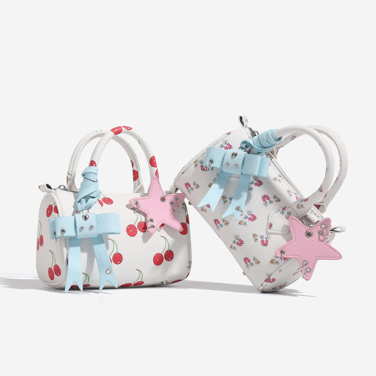 Mini white pebbled-finish Boston satchel with floral or cherry print, pastel blue bow charm, pink star charm, dual top, front