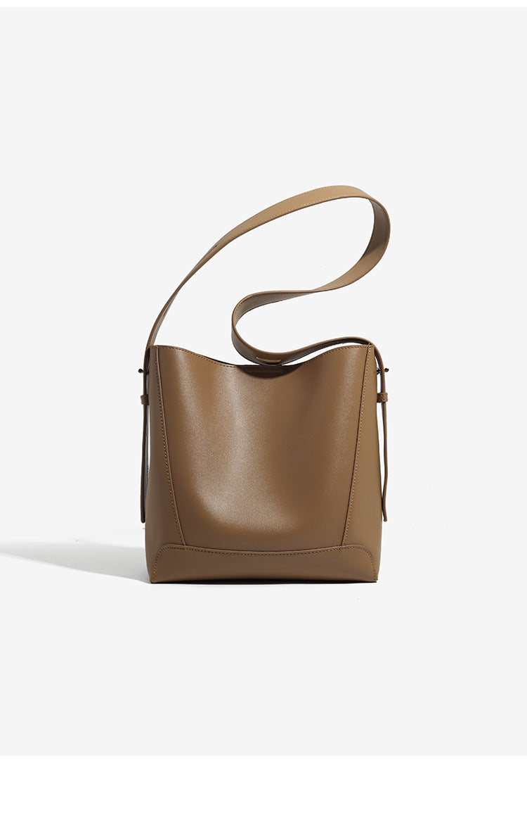 Structured smooth leather-look bucket shoulder bag with long adjustable strap and gold-tone buckle hardware in brown, detail