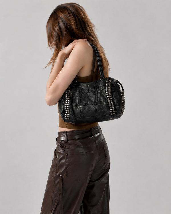 Black leather-look satchel bag with gunmetal rivet trim, grid-stitched paneling, dual rolled top handles, and curved zip