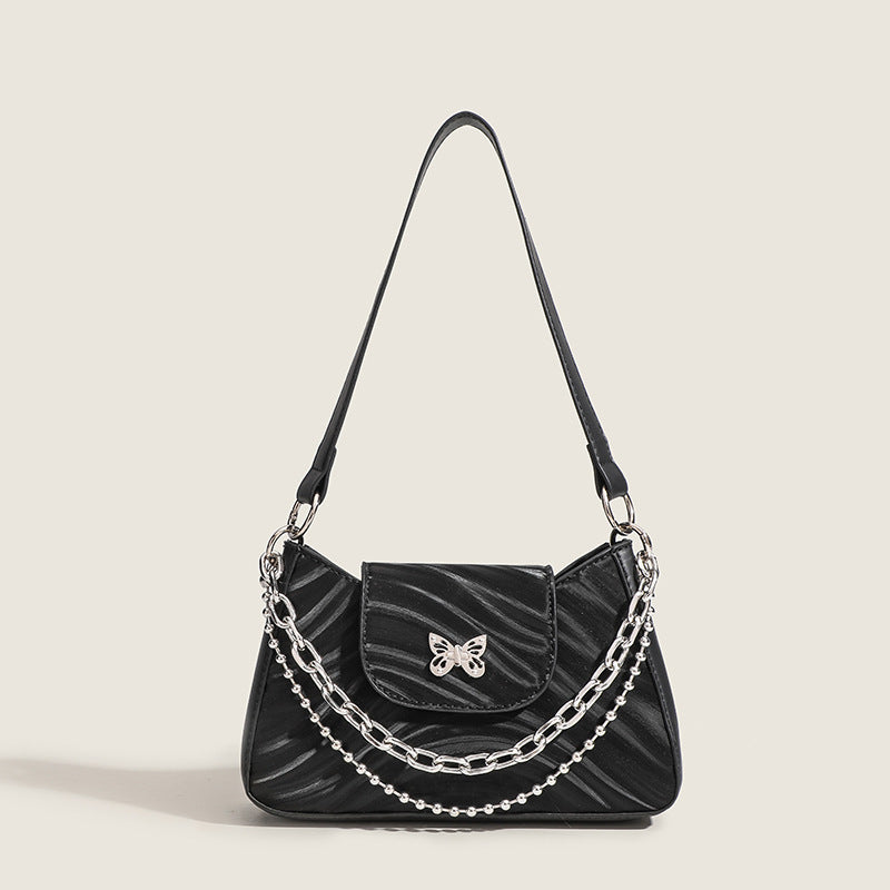 Kleine trapezförmige Schultertasche mit welliger Lederoptik, silberfarbenem Schmetterlingsverschluss vorne und mehrlagigem Kettenriemen mit Kugeldetails