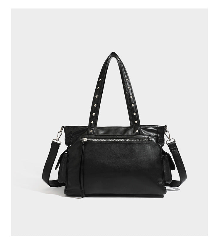 Black leather-look tote bag with silver pyramid studs on handles and front panel, multiple flap and zip exterior pockets