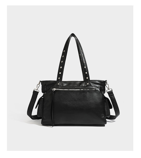 Black leather-look tote bag with silver pyramid studs on handles and front panel, multiple flap and zip exterior pockets