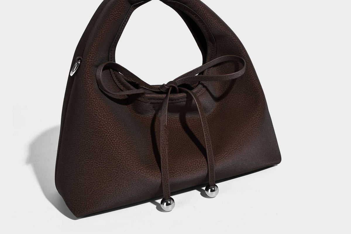 Pebbled matte trapezoid top-handle bag with drawstring bow closure, bead-tipped cords, silver-tone hardware, and detachable