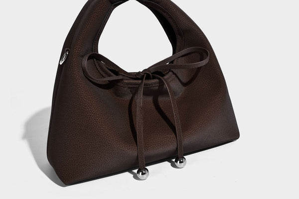 Pebbled matte trapezoid top-handle bag with drawstring bow closure, bead-tipped cords, silver-tone hardware, and detachable