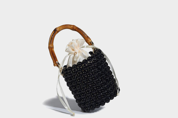Small cylindrical bucket bag with glossy faux-pearl bead exterior, bamboo arched top handle, satin drawstring closure, and
