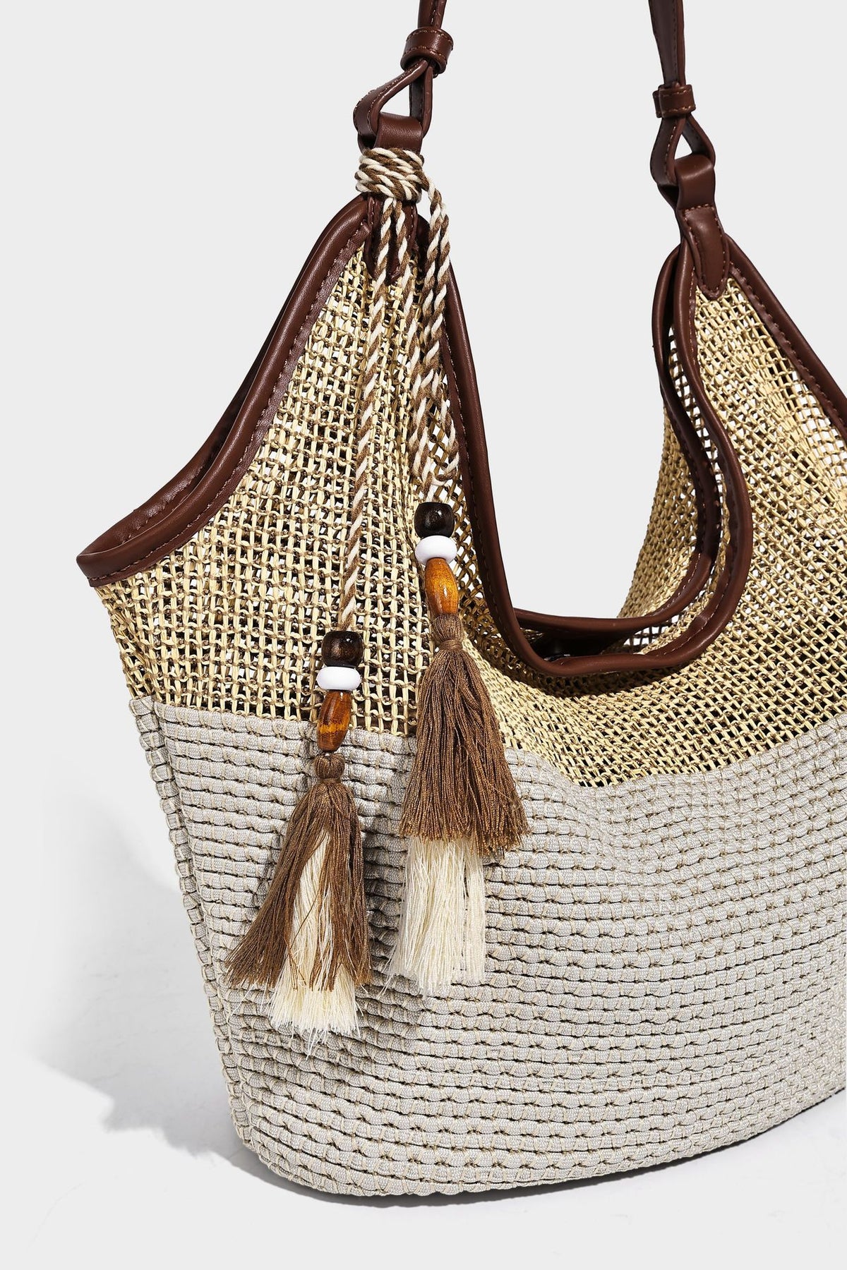 Two-tone beige and cream woven straw hobo shoulder bag with brown leather-look trim, long shoulder strap, and tassel-bead