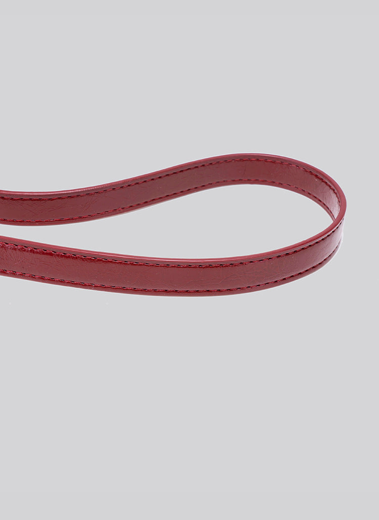 Glossy burgundy leather-look shoulder bag with curved gold-tone bar front closure, crinkled oil-wax texture, and adjustable