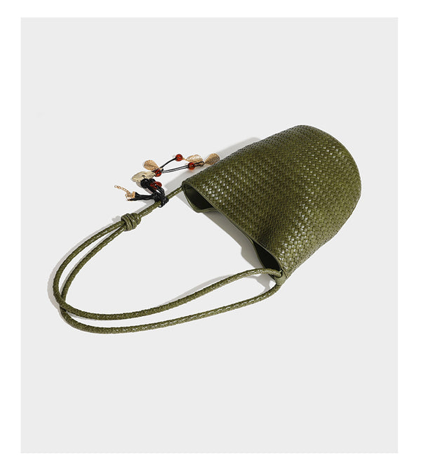 Olive green woven leather-look bucket bag with braided crossbody strap, knotted adjustment, and gold-tone tassel charm with