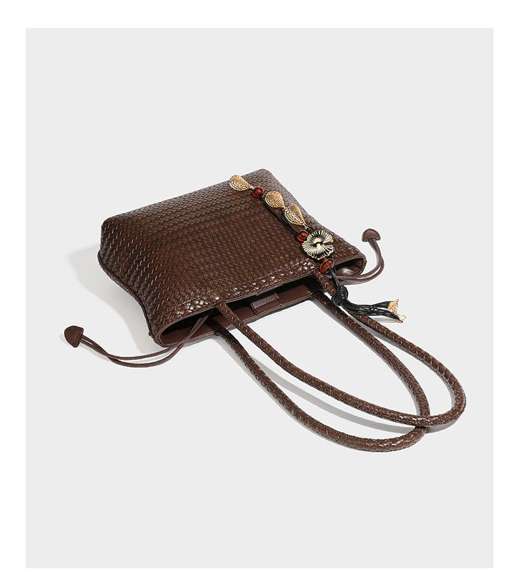 Structured woven leather-look tote bag in dark brown with long shoulder straps, side drawstring ties, and gold filigree
